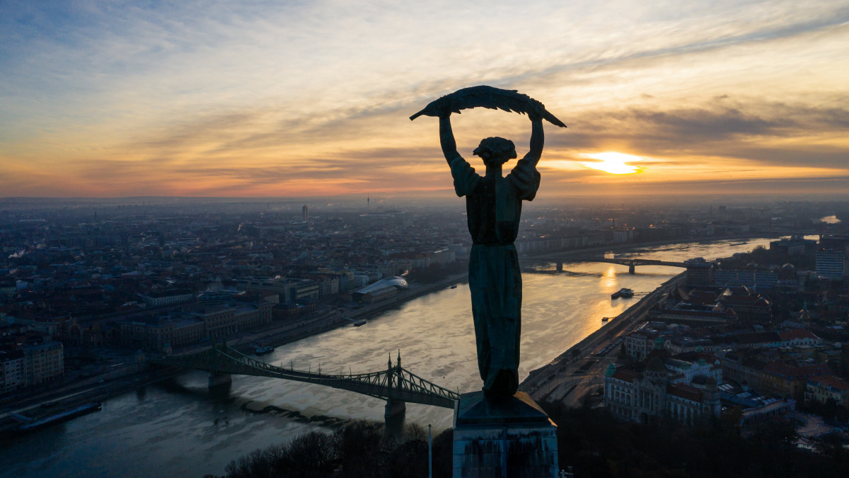 Budapest napfelkeltekor 2020. december 27-én. Az előtérben a Gellért-hegyi Szabadság-szobor, középen a Duna, a Szabadság híd és a Petőfi híd, jobbról az előtérben a Gellért Szálló látható.