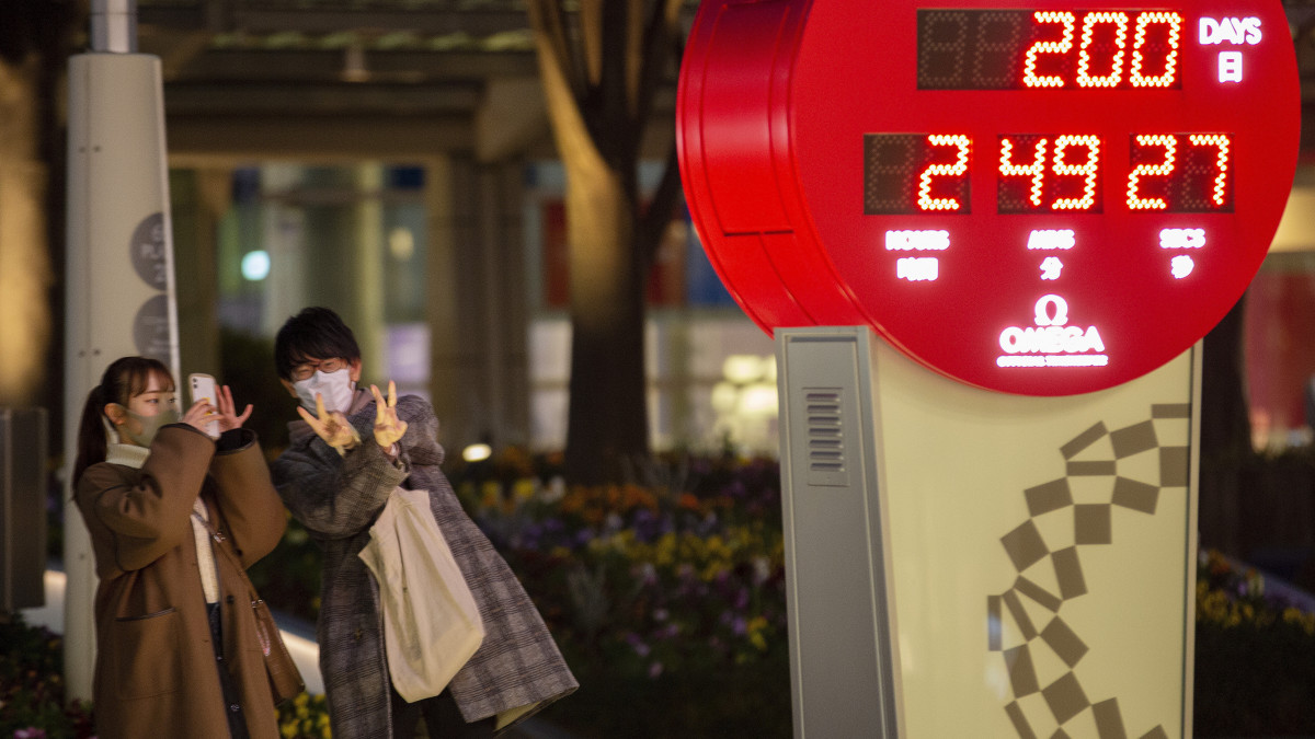 A tokiói olimpiáig még hátralévő időt számláló óra előtt fényképezkednek emberek a japán fővárosban 2021. január 4-én, pontosan kétszáz nappal a koronavírus-járvány miatt 2020-ról 2021-re halasztott nyári játékok kezdete előtt.