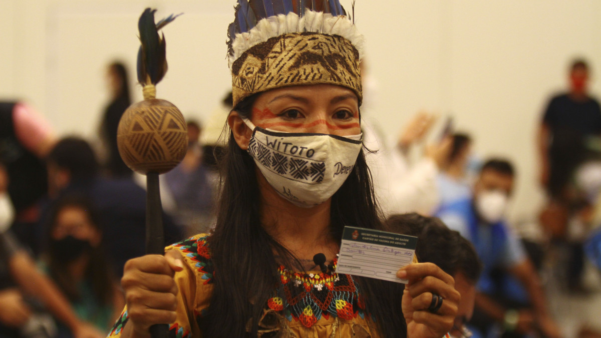 A Witoto őslakosok tradícionális öltözetét viselő Vanda Ortega egészségügyi dolgozó egy kártyát tart a kezében, amely igazolja, hogy beoltották a Sinovac Biotech kínai gyógyszergyártó cég koronavírus elleni vakcinájával az Amazonas állambeli Manausban 2021. január 18-án.