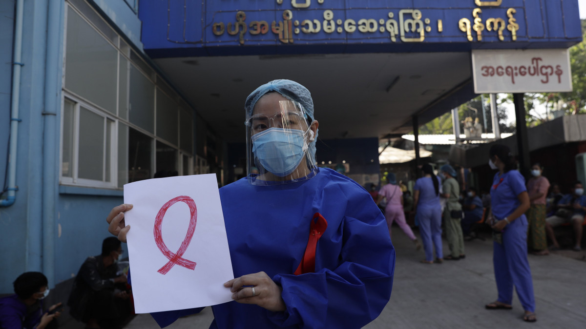 Piros szalagot visel védőruházatán egy egészségügyi dolgozó az előző napokban végrehajtott katonai hatalomátvétel elleni tiltakozás jeléül a ranguni Központi Női Kórház előtt 2021. február 3-án. Egy civil engedetlenségi mozgalom Facebookon közzétett bejelentése szerint Mianmarban hetven kórház egészségügyi személyzete lépett sztrájkba, mert véleményük szerint a katonaság saját érdekeit a koronavírus-járvánnyal küzdő emberek érdekei elé helyezi.