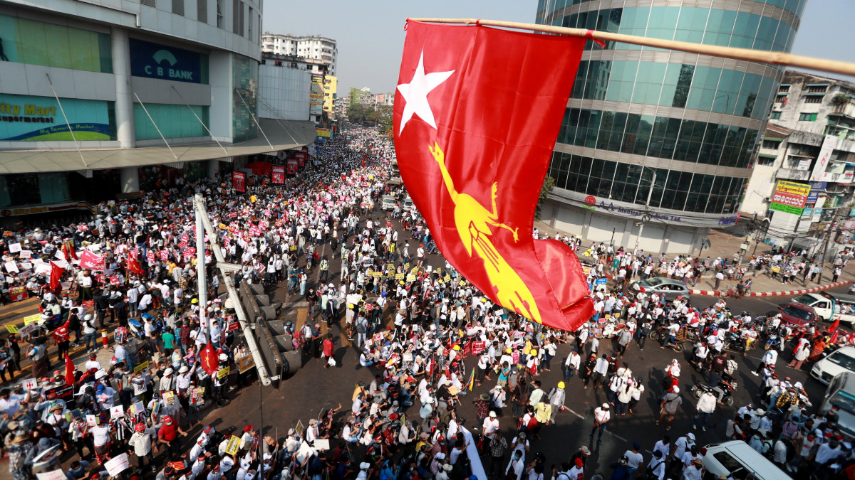 Az Aung Szan Szú Kjí államtanácsos vezette Nemzeti Liga a Demokráciáért (NLD) párt zászlaja leng a katonai hatalomátvétel miatt tiltakozó tüntetők menete felett Rangunban 2021. február 22-én. A tüntetők a polgári kormányzás visszaállítását, az őrizetbe vettek szabadlábra helyezését és a katonáknak kedvező alkotmány eltörlését követelik.
