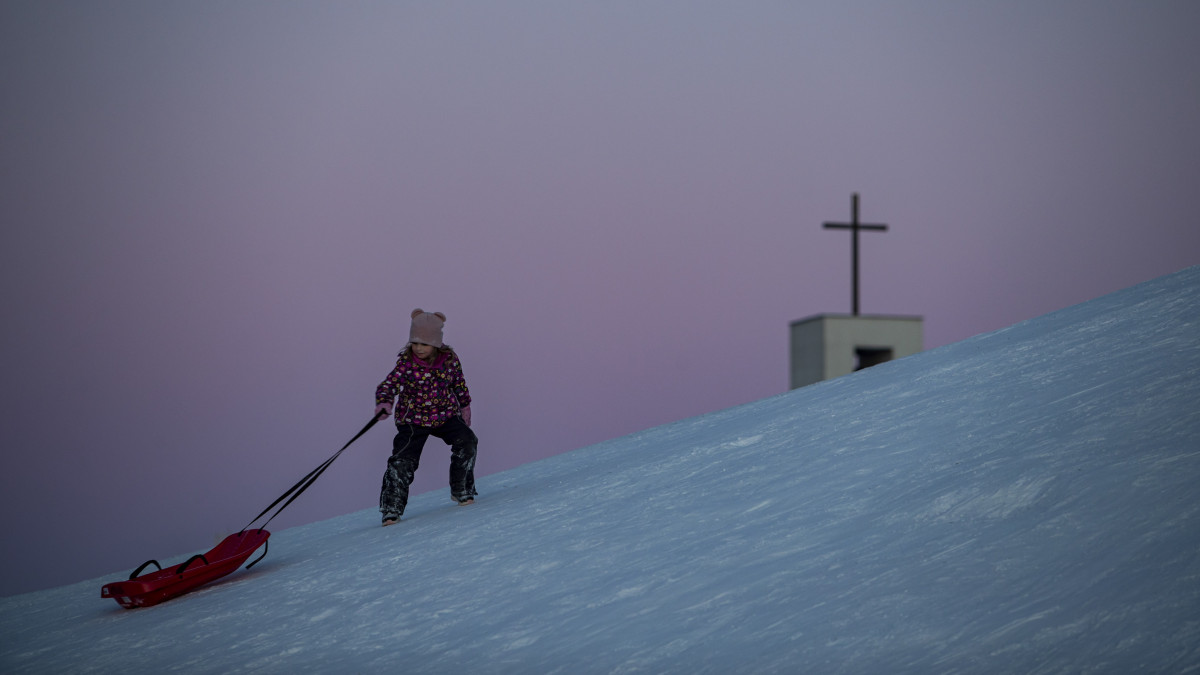 A szánkóját húzza egy kislány a hóval borított domboldalon Prágában 2021. február 14-én.