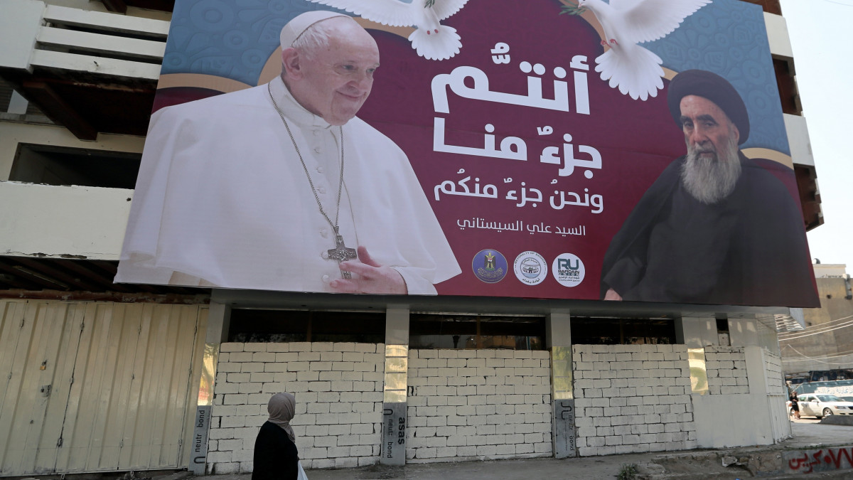 Nő halad el egy Ferenc pápát (b) és Ali al-Szisztánit, az iraki síiták legjelentősebb vallási vezetőjét ábrázoló plakát előtt Bagdadban 2021. március 1-jén. Ferenc pápa a tervek szerint március 5. és 8. között látogat Irakba.