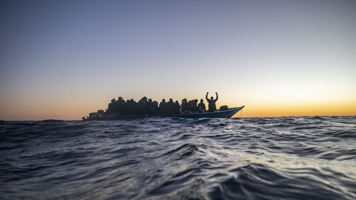Afrikai országokból indult illegális bevándorlók egy túlzsúfolt csónakban várják az Open Arms spanyol nem kormányzati szervezet hajóját a Földközi-tengeren, a líbiai partoktól mintegy 122 mérföldre 2021. február 12-én.
