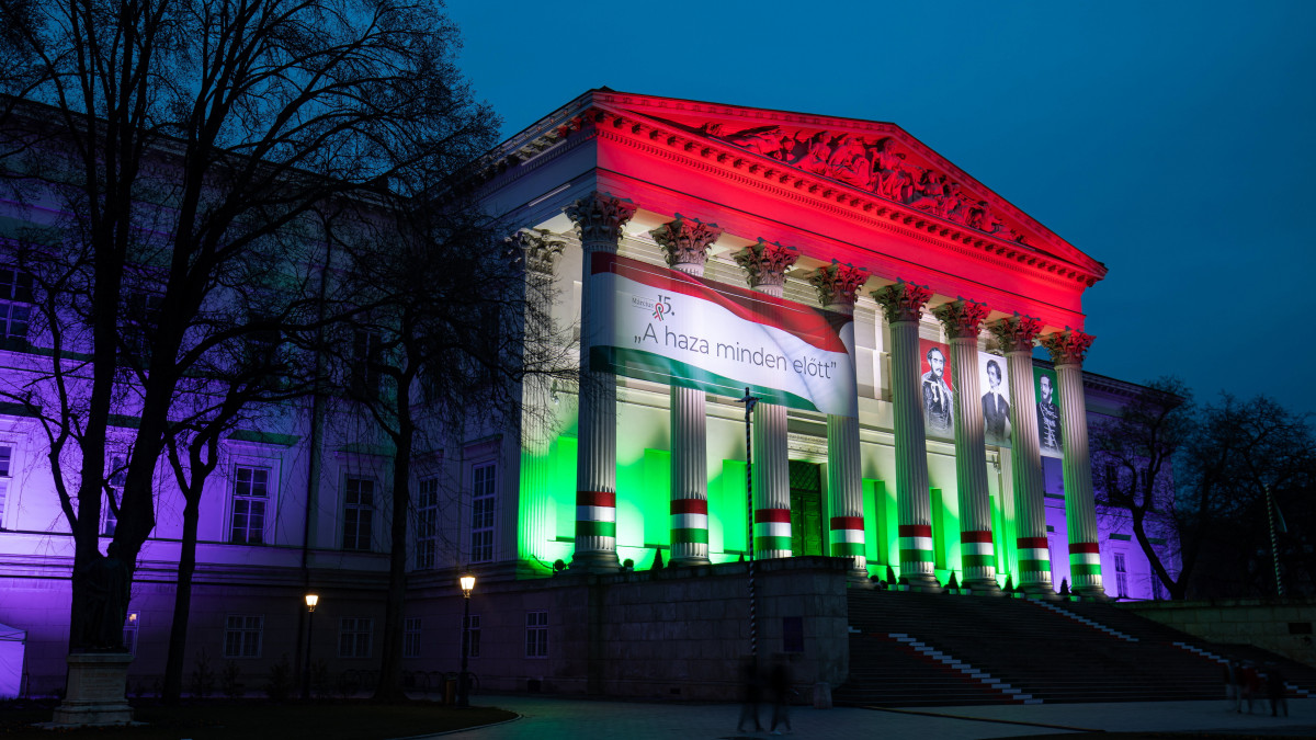 A nemzeti ünnep tiszteletére feldíszített Magyar Nemzeti Múzeum épülete esti díszkivilágításban 2021. március 13-án. A koronavírus-járvány miatt elmaradnak a március 15-ei ünnepségek, csak a zászlófelvonást tartják meg reggel 8 órakor az Országház előtti Kossuth Lajos téren.