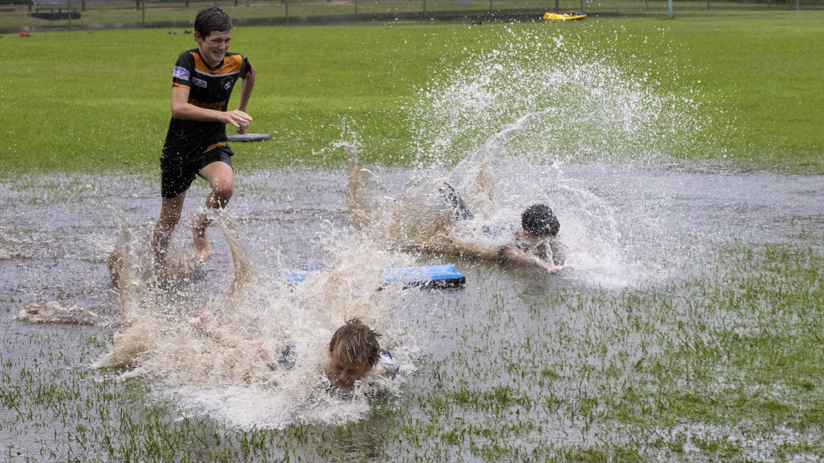 Gyerekek játszanak egy árvízben álló parkban Sydneytől mintegy 200 km-re északra, Port Stephens városban 2021. március 20-án. A várható további heves esőzések miatt  Új-Dél-Wales állam tengerparti szakaszára árvízveszélyre szóló figyelmeztetést adtak ki.