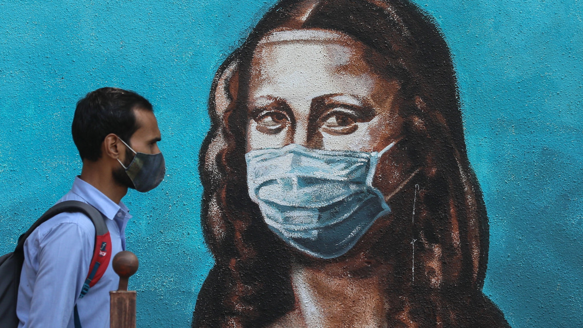 A koronavírus-járvány miatt védőmaszkot viselő férfi halad el egy falfestmény előtt, amely Leonardo da Vinci olasz festő Mona Lisáját ábrázolja védőmaszkkal az arcán az indiai Mumbaiban 2021. március 17-én. Indiában az elmúlt két napban regisztrálták a legtöbb új fertőzöttet ebben az évben.