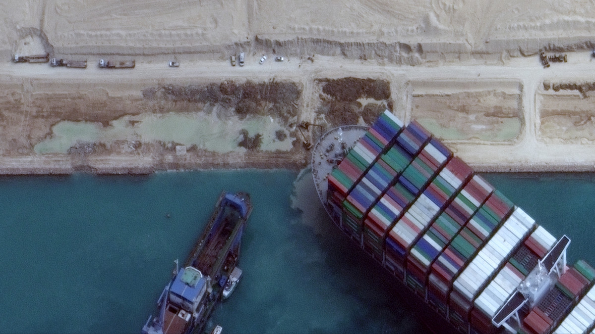 A Maxar Technologies által közreadott műholdfelvételen munkagépekkel és vontatóhajókkal próbálják kiszabadítani a keresztbe fordult és beszorult Ever Given nevű konténerszállítót a Szuezi-csatornában 2021. március 28-án. A világ egyik legnagyobb teherhajója öt napja blokkolja a forgalmat, a baleset miatt felfüggesztették a hajóforgalmat a Szuezi-csatornában.