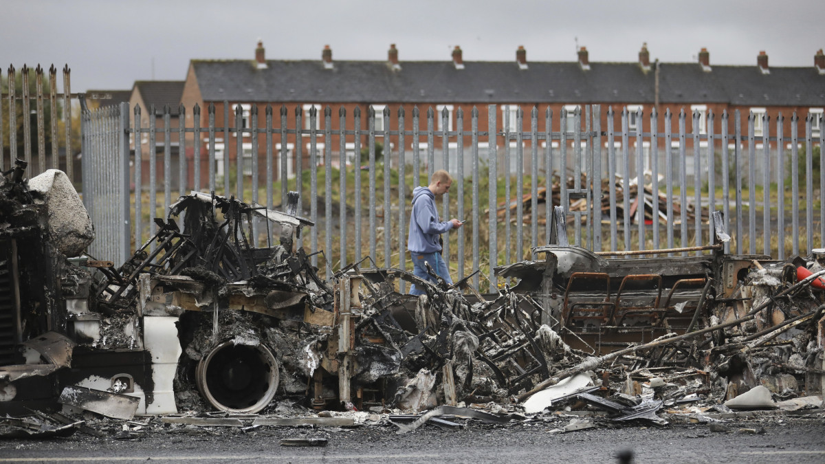 Férfi halad el egy kiégett busz maradványai mellett Belfast nyugati részén 2021. április 7-én. A rendőrségnek le kellett zárnia a nacionalista katolikusok és a lojalista protestánsok lakta területeket összekötő utakat, miután egyre nagyobb területre terjedtek ki az erőszakos cselekmények.