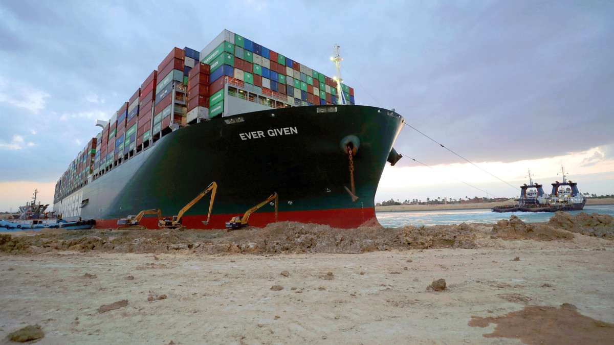 A Szuezi-csatorna Hatóság által közreadott képen vontatóhajókkal és munkagépekkel próbálják kiszabadítani a keresztbe fordult és beszorult Ever Given nevű konténerszállítót a Szuezi-csatornában 2021. március 28-án. A világ egyik legnagyobb teherhajója öt napja blokkolja a forgalmat, a baleset miatt felfüggesztették a hajóforgalmat a Szuezi-csatornában.