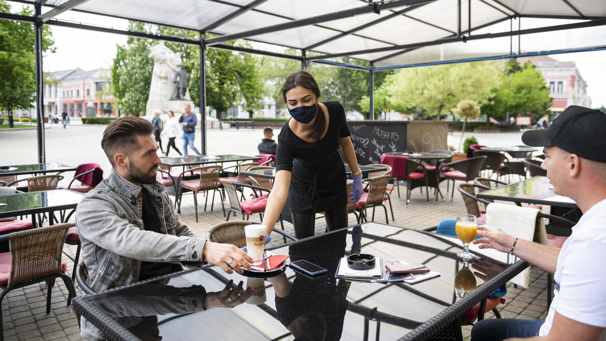 Felszolgáló kiviszi a rendelést a vendégeknek egy kávézó teraszán Nyíregyházán a Kossuth téren 2020. május 4-én. A koronavírus-járvány miatti korlátozások Budapesten és Pest-megyén kívüli részleges feloldása értelmében vidéken ismét kinyithattak az éttermek és kávézók teraszai, kerthelyiségei.