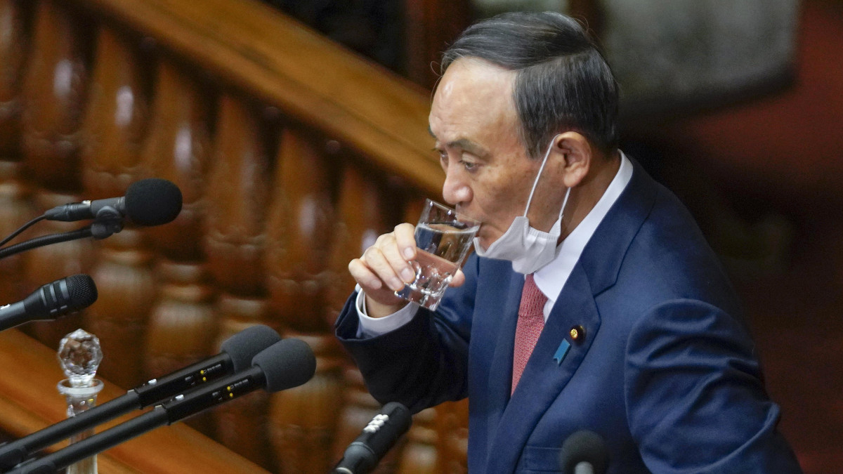Szuga Josihide japán miniszterelnök vizet kortyol, mielőtt képviselői kérdésekre válaszol a parlament alsóházának 2021. január 20-i ülésén Tokióban. Az ülés központi témái a koronavírus-járvány elleni védekezésre irányuló kormányintézkedések és a vírus világjárványa miatt 2020-ról 2021-re halasztott tokiói nyári olimpia voltak.