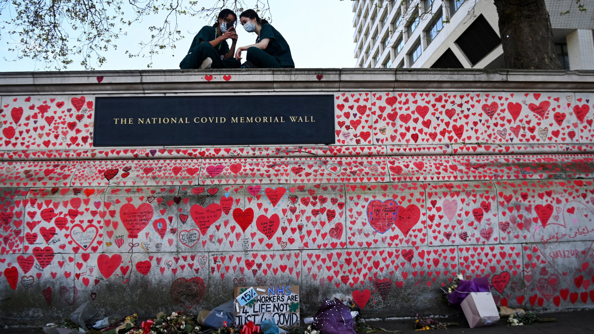 Két ápolónő beszélget a koronavírus-járvány brit áldozatai tiszteletére kialakított emlékfal tetején London belvárosában 2021. április 27-én. A piros szíveket március 29-én kezdték el felrajzolni a falra az elhunytak hozzátartozói.