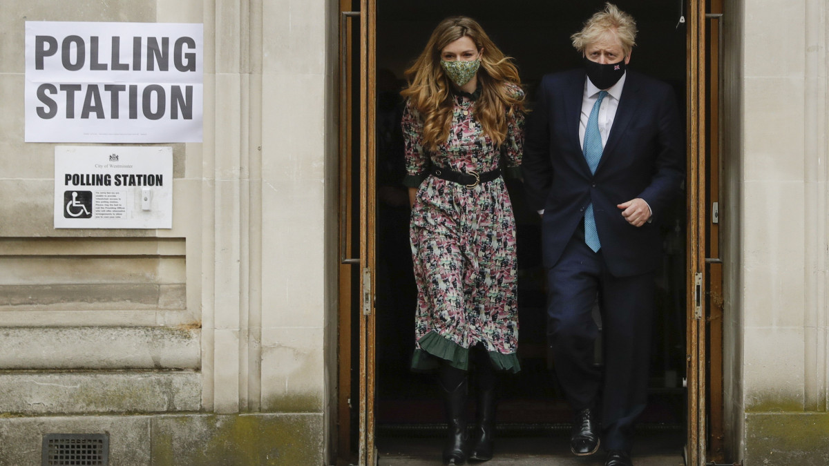 Boris Johnson brit miniszterelnök az élettársa, Carrie Symonds társaságában távozik egy londoni szavazóhelyiségből az angliai helyhatósági választásokon 2021. május 6-án.