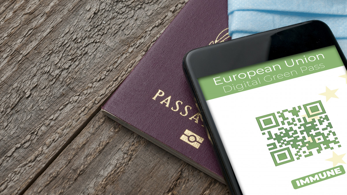Digital Green Pass concept: Smartphone over a passport and a surgical mask on a wooden table show an hypotetical app for the Digital Green Passport (or digital pass certificate)