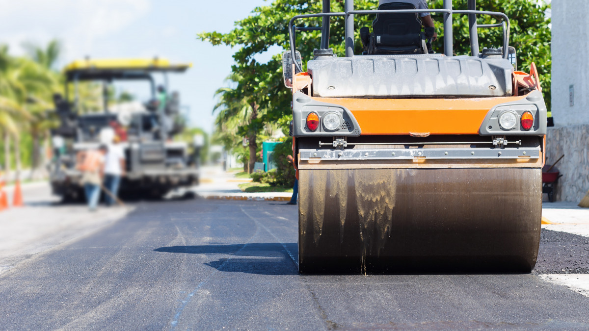 Road construction works with steamroller machine and asphalt finisher