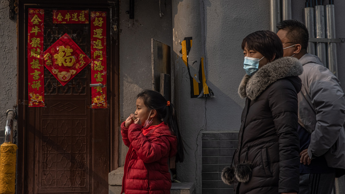 A koronavírus-járvány miatt védőmaszkot viselő család egy holdújévre feldíszített ajtó előtt, Peking Hutung negyedében 2021. február 11-én, a legnagyobb kínai ünnep előestéjén. A holdújévvel idén az állatövek szerint jelölt tizenkét esztendő közül a bivaly éve kezdődik.