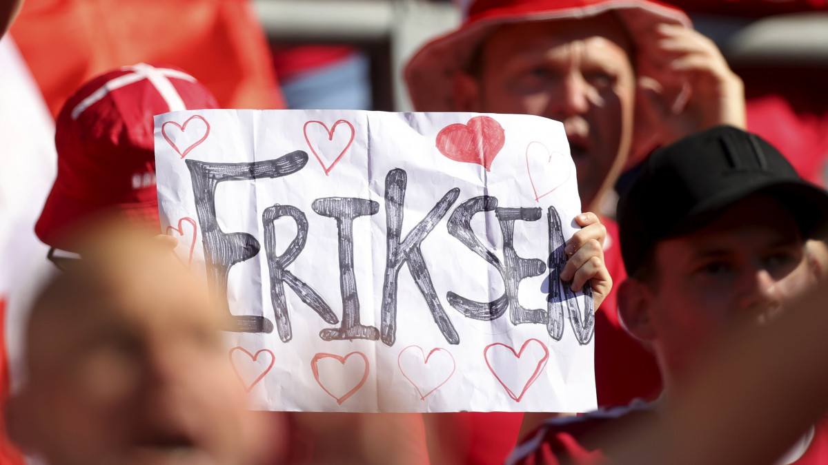 Christian Eriksennek, a dán labdarúgó-válogatott csapatkapitányának üzen a kezében egy papírt tartó szurkoló a lelátón a koronavírus-járvány miatt 2021-re halasztott 2020-as labdarúgó Európa-bajnokság B csoportjának második fordulójában játszott Dánia-Belgium mérkőzés előtt Koppenhágában 2021. június 17-én. Eriksen június 12-én az Eb-újonc finnek elleni összecsapás 43. percében mindenféle előzmény nélkül összeesett a pályán, ahol bő tíz percen keresztül élesztették újra, mielőtt szállítható állapotba került. A 109-szeres válogatott játékost végül stabil állapotban vitték kórházba, ahol már kommunikálni is tudott.
