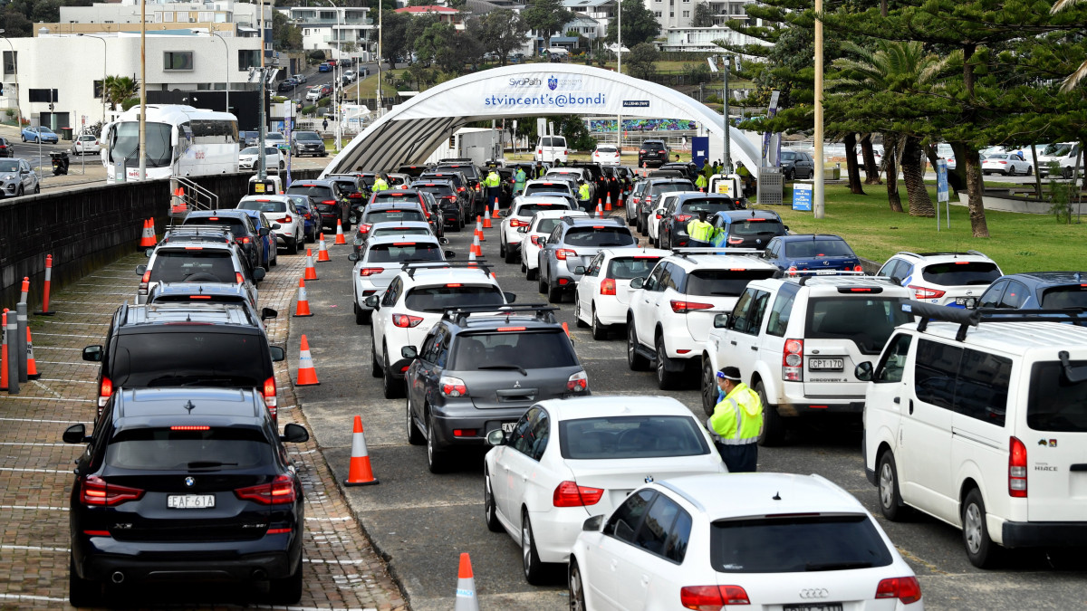 Koronavírus-tesztre váró emberek egy autós tesztállomáson Bondiban, Sydney egyik elővárosában 2021. június 22-én. Ebben a gócpontban az azonosított fertőzöttek száma elérte a 21 főt, ezért kötelezővé tették a védőmaszk viselését tömegközlekedési eszközökön és a zárt vendéglátó egységekben.