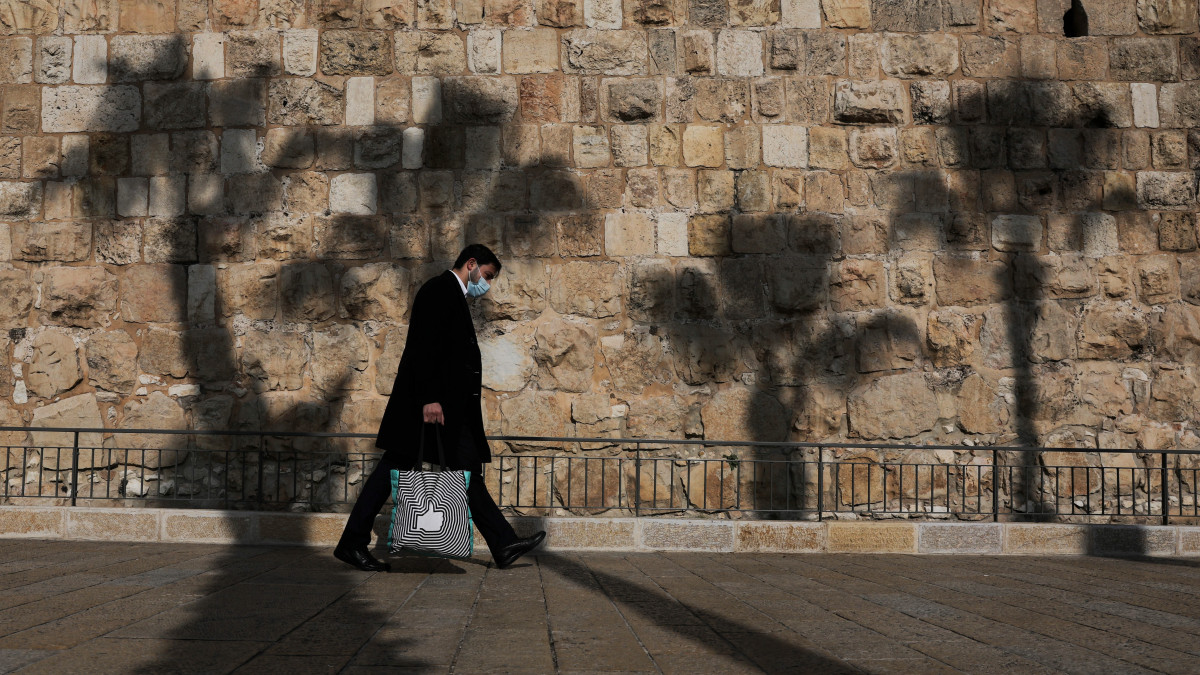 A koronavírus-járvány miatt védőmaszkot viselő férfi halad el Jeruzsálem óvárosának fala mellett 2020. november 30-án. A több hónapig tartó kijárási korlátozásokat követően Izraelben újra kinyitottak a bevásárlóközpontok.