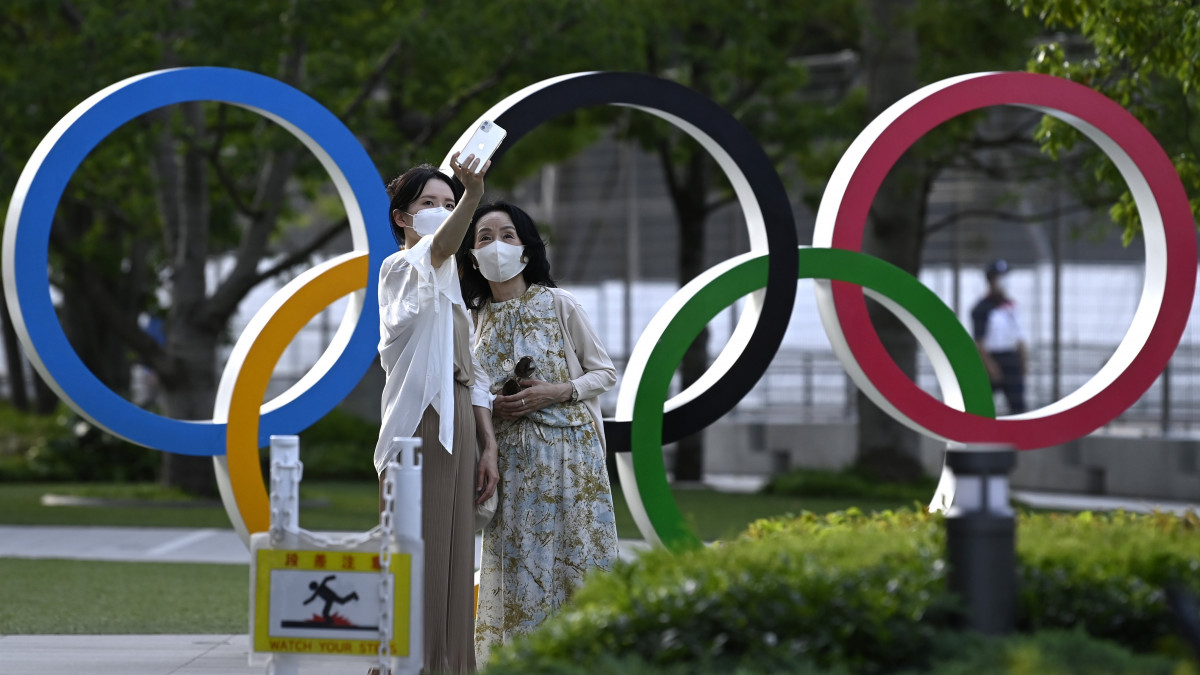 Helyiek fényképezkednek az olimpiai ötkarika előtt a megnyitóünnepség helyszíne, a tokiói Olimpiai Stadion közelében 2021. július 15-én. A világméretű koronavírus-járvány miatt 2021-re halasztott 2020-as tokiói nyári olimpia július 23-án kezdődik.