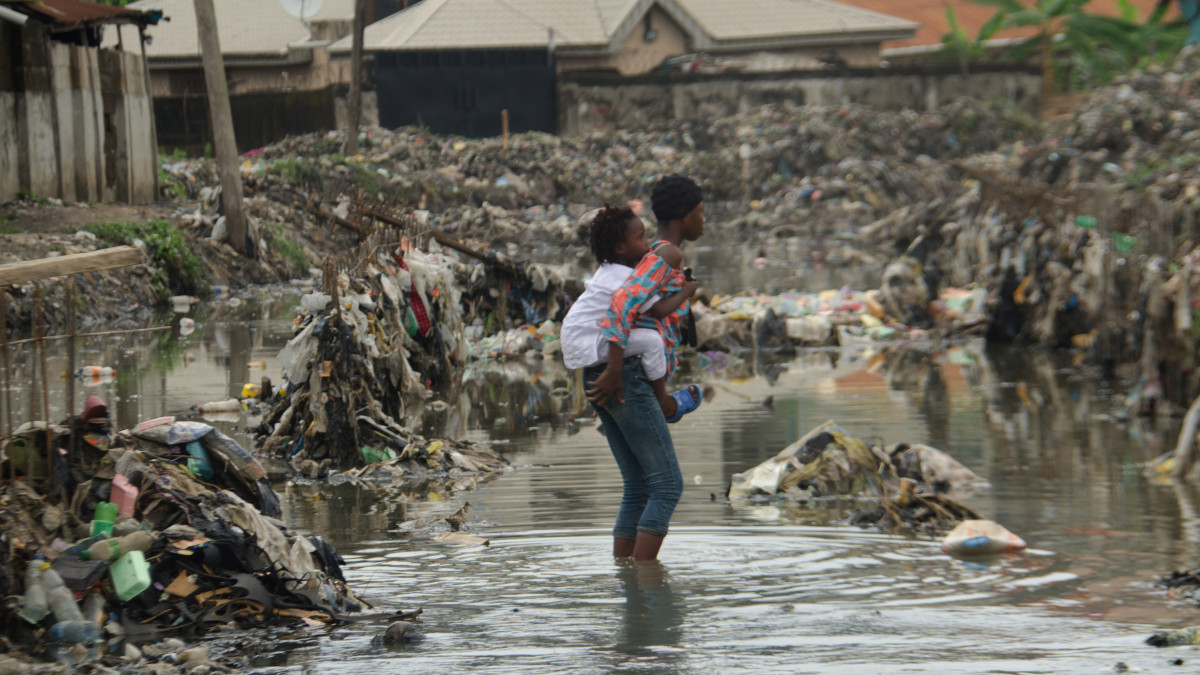 A girl carries her young brother on her back as they walk through a flooded cannal, following rain fall at Oyebanjo Solarin Street in Ketu, Lagos which washed away a two yet to be identified children, after a heavy rainfall on Saturday in Lagos, on September 13, 2020.     (Photo by Olukayode Jaiyeola/NurPhoto via Getty Images)