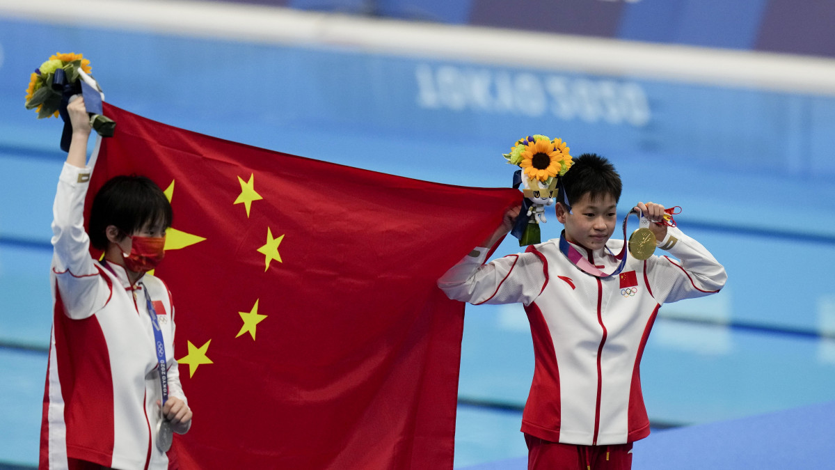 Az ezüstérmes kínai Csen Jü-hszi  (b) és aranyérmes honfitársa, Csüan Hung-csan ünnepel a világméretű koronavírus-járvány miatt 2021-re halasztott 2020-as tokiói nyári olimpia női 10 méteres műugrásának eredményhirdetésén a Tokiói Vizesközpontban 2021. augusztus 5-én.