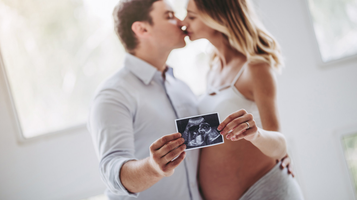 Happy couple spending time together. Attractive pregnant woman with her husband at home holding ultrasound image in hands. Ultrasonography. Last months of pregnancy.