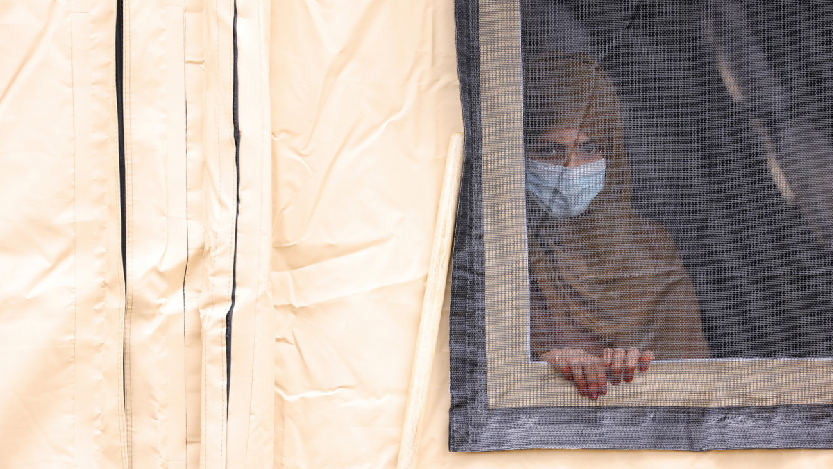 RAMSTEIN-MIESENBACH, GERMANY - AUGUST 26: A woman looks out through a window from a temporary emergency shelter for the evacuees from Afghanistan at the Ramstein Air Base on August 26, 2021 in Ramstein-Miesenbach, Germany. Ramstein has become one of the main preliminary destinations for evacuees leaving Afghanistan on U.S. military flights. U.S. forces there have built a temporary shelter and are preparing to accept up to 10,000 people. Evacuations by a multitude of nations of their citizens and endangered Afghans are ongoing as the Taliban warn against extending foreign military presence in Afghanistan beyond August 31. (Photo by Andreas Rentz/Getty Images)