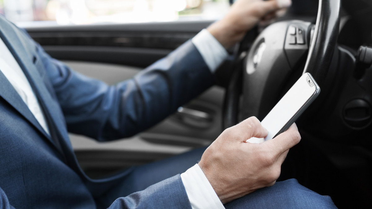 Businessman ignoring safety, texting on smartphone and driving car, cropped