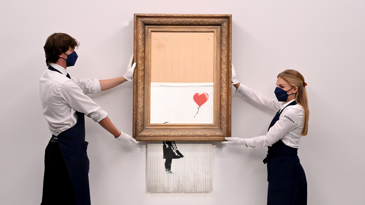 2021. szeptember 3-án készített kép, amelyen a Sothebys aukciós ház munkatársai Banksy brit graffitiművész Love is in the Bin című alkotását fogják a cég londoni kiállítótermében. Az eredetileg Girl With Balloon című képet először 2018 októberében árverezték el Londonban 1,4 millió euróért, akkor a leütés után a képkeretbe épített iratmegsemmisítő félig csíkokra szabdalta a festményt, most pedig új címével október 14-én bocsátották licitálásra, a leütési ára 18,6 millió font (kb. 7,875 milliárd forint) lett, a legmagasabb ár, amit Banksy-képért fizettek.