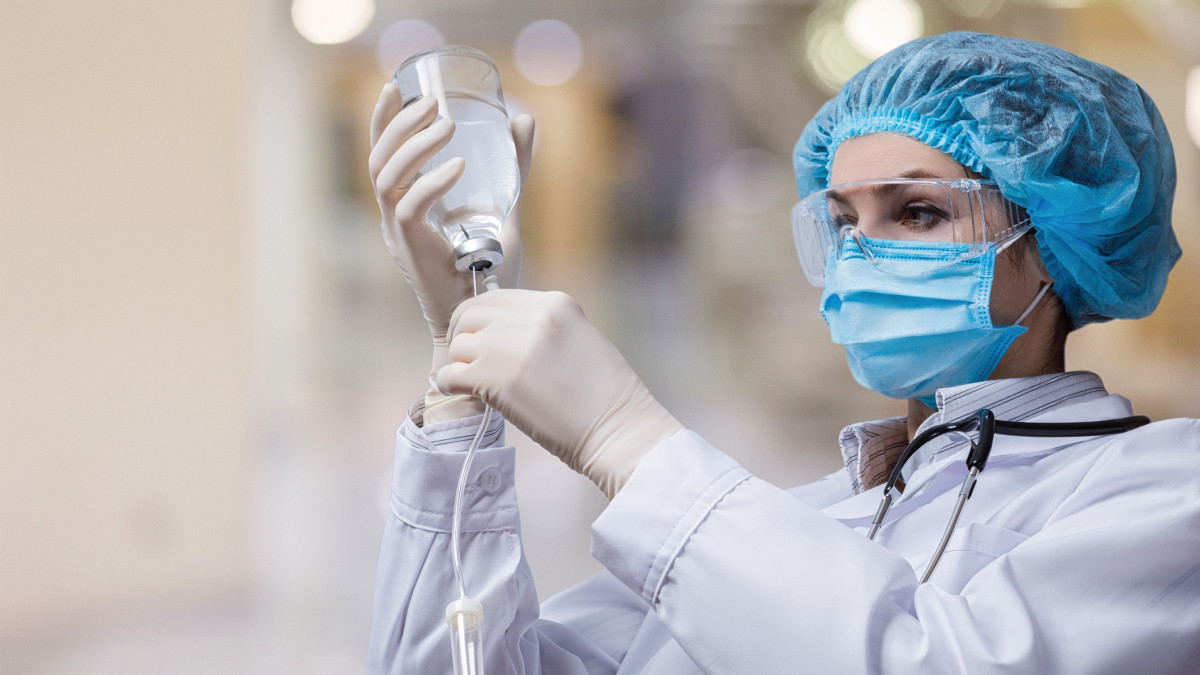 The doctor prepares a system for transfusion of infusion solutions on a blurred background.