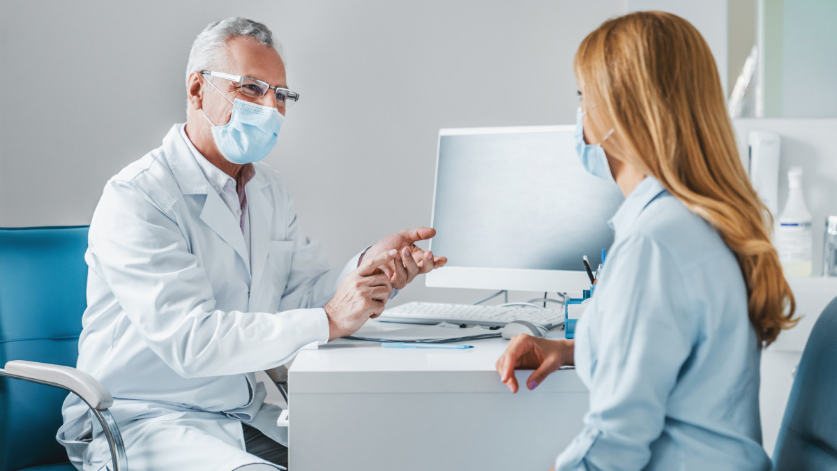 Senior male doctor wear protection face mask talking with patient in clinic office