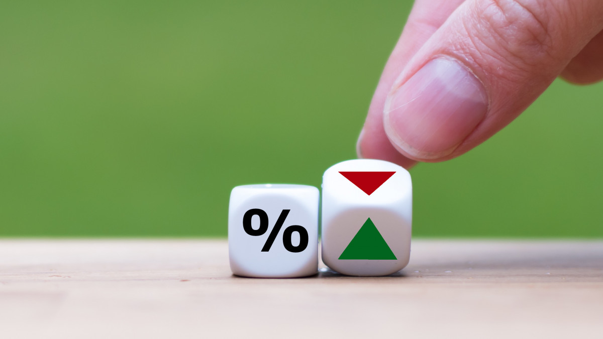 Hand is turning a dice and changes the direction of an arrow symbolizing that the interest rates are going down (or vice versa)