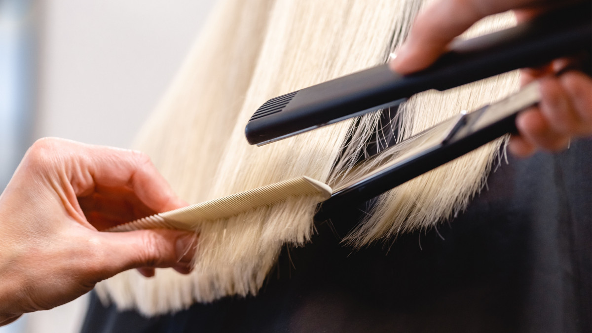 Hairdresser using a flat iron hair straightener to straighten womans blonde hair