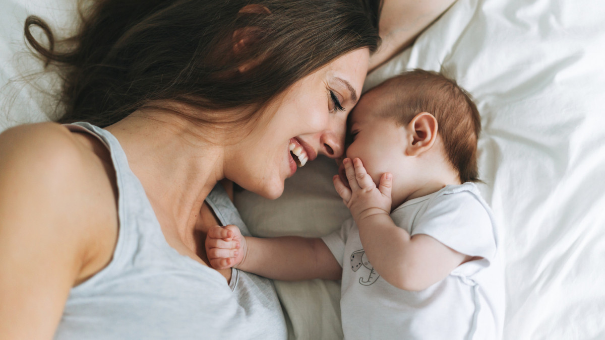 Young mother having fun with cute baby girl on bed, natural tones, love emotion