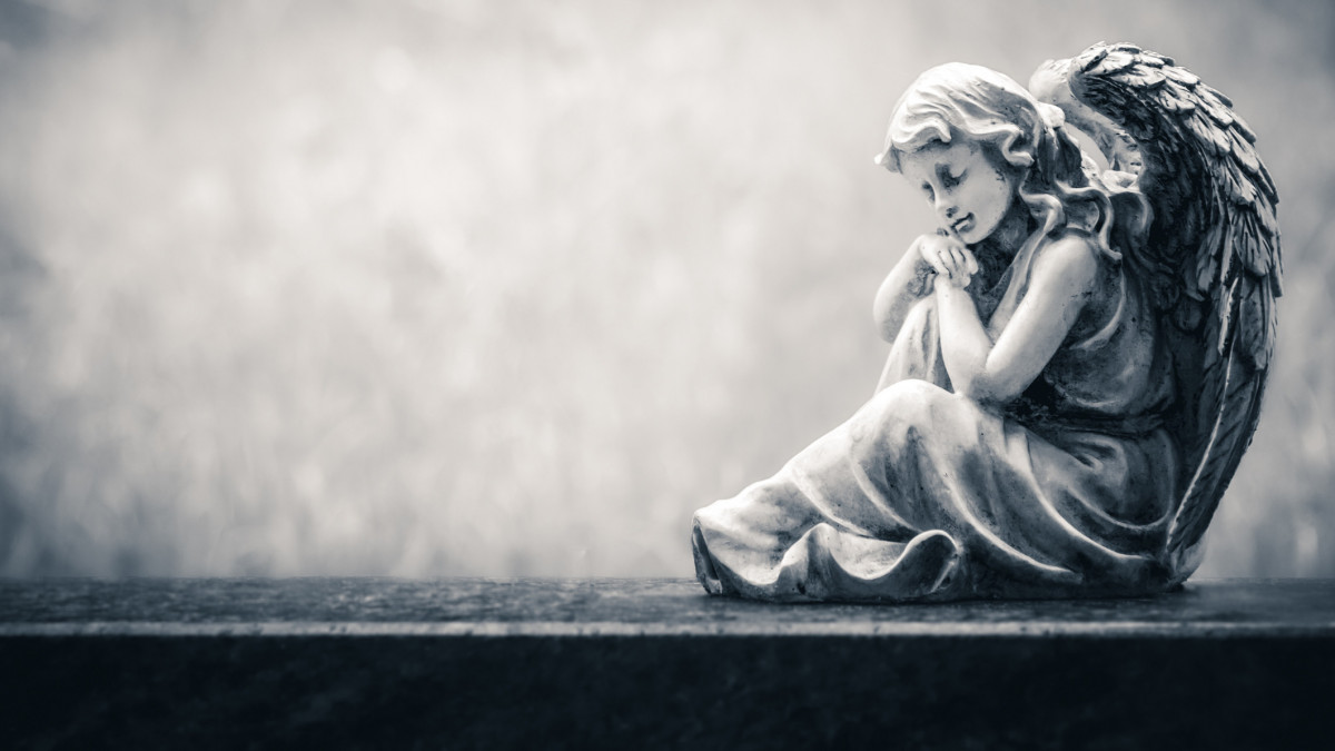 Angel figure sitting on an old headstone in a cemetery. Vintage, retro monochrome image with copy space. Halloween, all saints background concept.