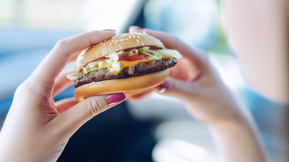 Girl holding a hamburger in  her hands sitting in a car. Unhealthy eating concept - shallow depth of field