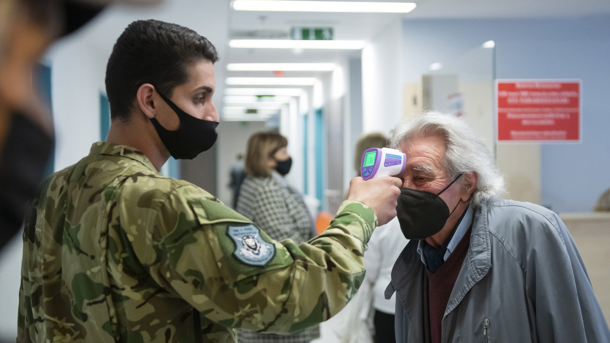 Egy katona megméri egy férfi testhőmérsékletét, mielőtt belép a nyíregyházi Jósa András Oktatókórházban kialakított oltópont folyosójára 2021. május 1-jén.