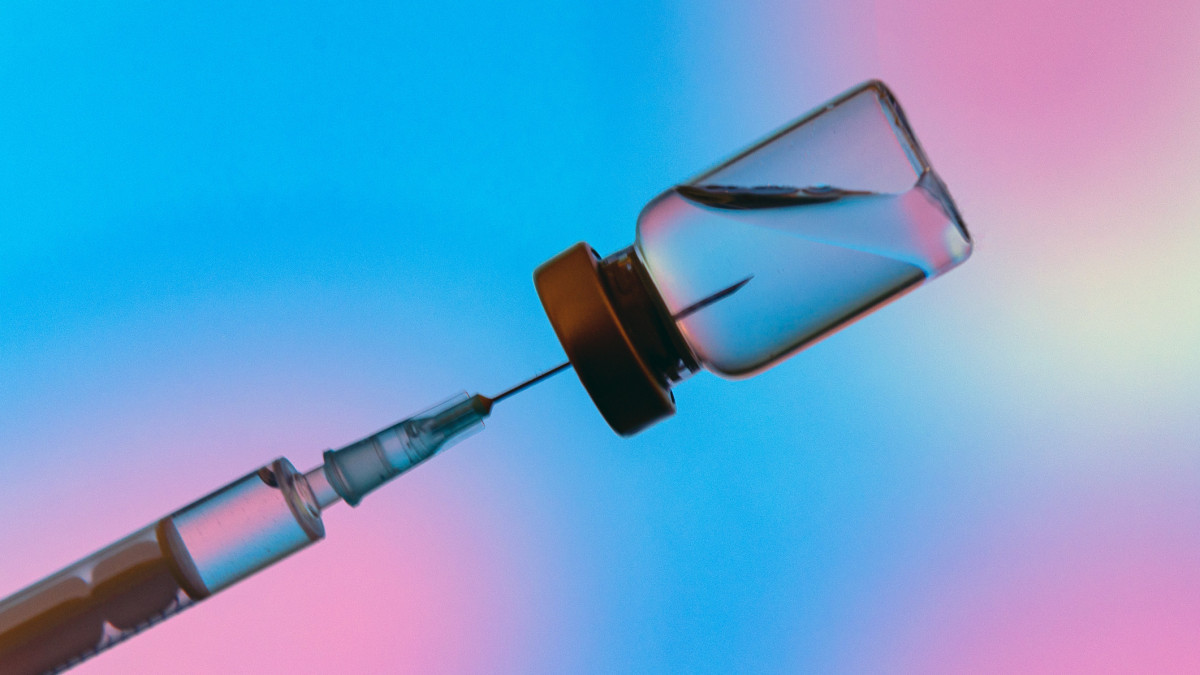 Injection vial with syringe needle on blue and purple background. Coronavirus vaccine ready for worldwide administration.