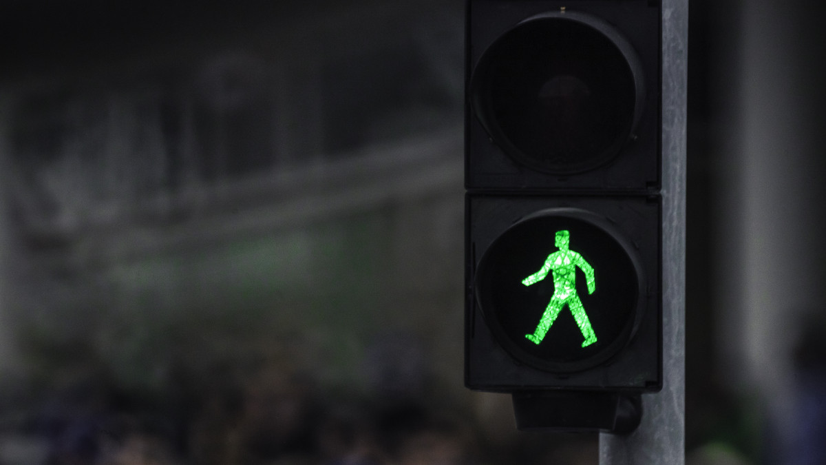 A sidewalk crossing light in Reykjavik, we see the walking icon on the lamp, this is in the street of the city, the light is of color green.  This is a close up of the traffic signal.