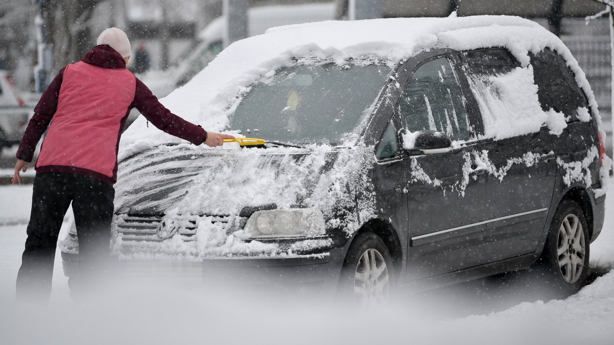 Nő havat söpör le egy autóról Debrecenben 2021. december 13-án.
