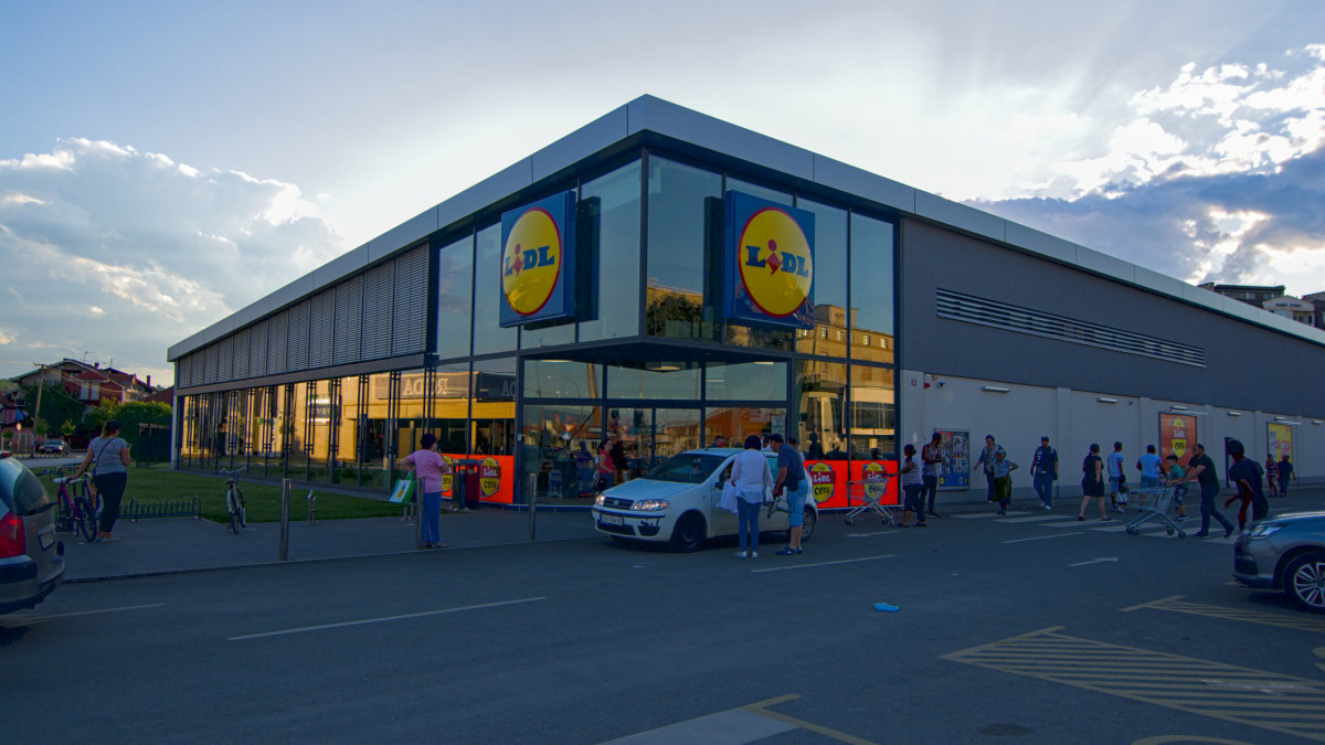 Cars move in the parking lot in front of the entrance to the Lidl supermarket building