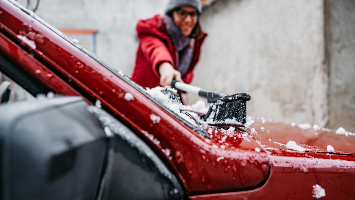 Young woman cleaning snow off her car in backyard.