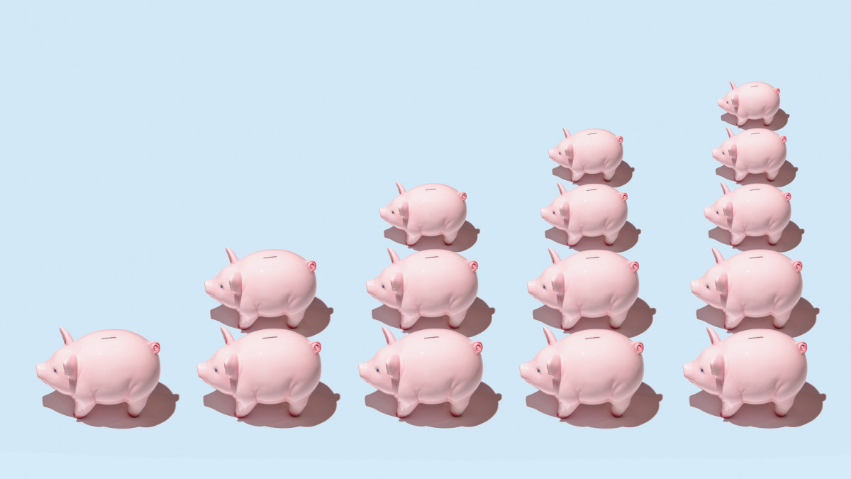 Differently sized pink ceramic piggy banks in stacks forming a bar graph on blue surface