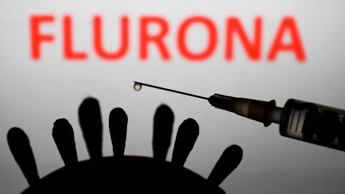 Coronavirus model, medical syringe and flurona sign displayed in the background are seen in this illustration photo taken in Poland on January 4, 2022. Some countries reported cases of patients that were infected both COVID-19 and flu. (Photo by Jakub Porzycki/NurPhoto via Getty Images)