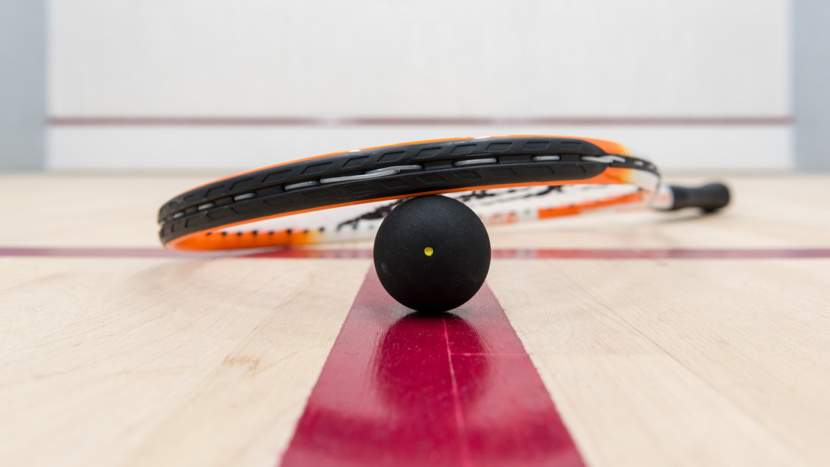 Squash racket and 1-spot ball lying on the floor of an empty squash court