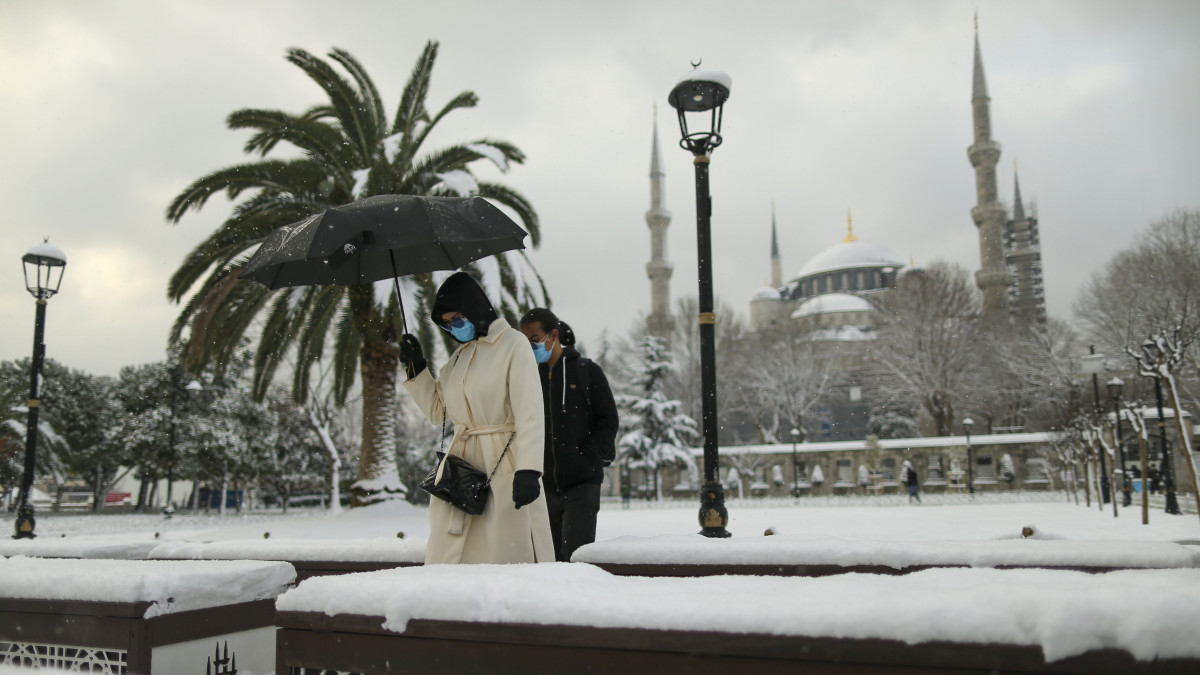 A koronavírus-járvány miatt védőmaszkot viselő emberek mennek egy hóval borított téren, az isztambuli Kék mecset előtt 2022. január 24-én.