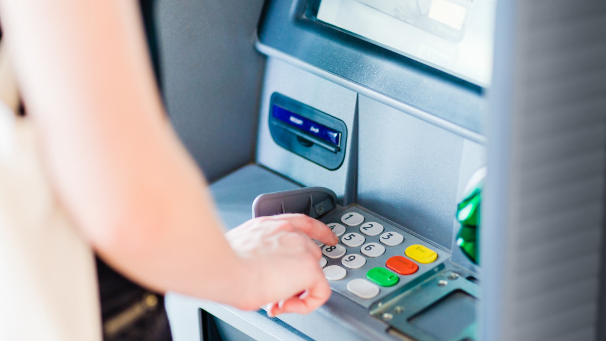 Closeup of a caucasian adult person pressing on ATM machine keypad number to withdraw cash money.