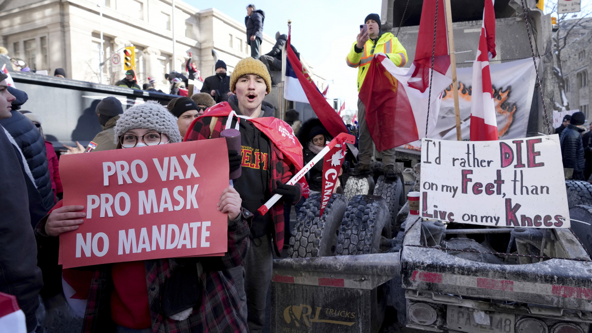 Táblát tart a koronavírus elleni oltást és a maszkviselést támogató, de az oltás kötelezővé tételét ellenző tüntető (b) a járványügyi korlátozások ellen tiltakozó kamionosokat támogató felvonuláson Ottawában 2022. február 5-én. A tüntetés azután robbant ki, hogy január 15-én életbe lépett a kanadai kormány rendelkezése, amely védőoltás hiányában 14 napos karanténra kötelezi az Egyesült Államokból érkező kamionosokat.